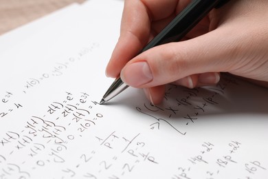 Photo of Student writing different mathematical formulas on paper, closeup