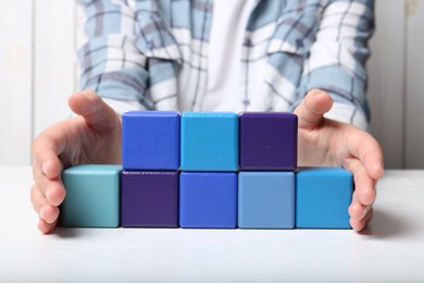 Photo of Woman demonstrating empty colorful cubes at white table, closeup. Space for design