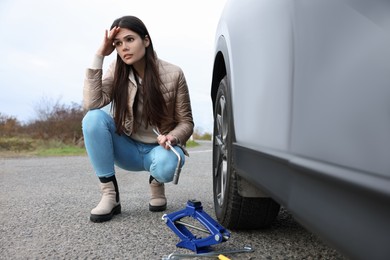 Worried young woman near car with punctured wheel on roadside