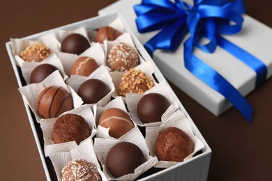 Photo of Box with delicious chocolate candies on brown background, closeup