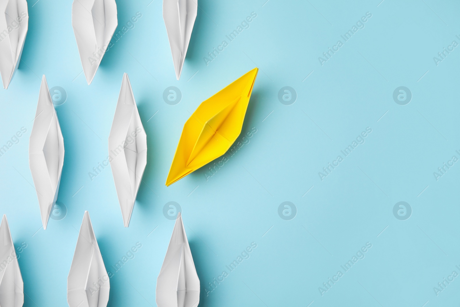 Photo of Yellow paper boat floating away from others on light blue background, flat lay with space for text. Uniqueness concept