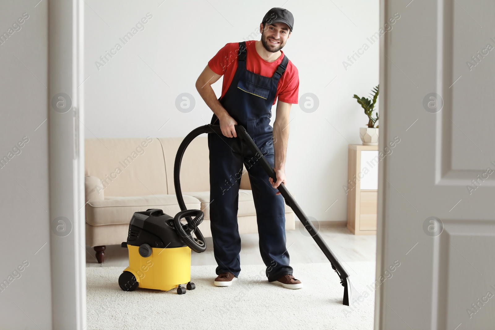 Photo of Male worker cleaning carpet with vacuum in living room