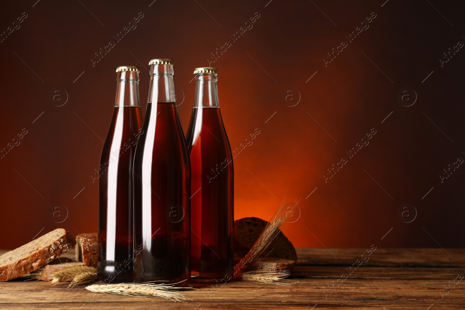 Photo of Bottles of delicious fresh kvass, spikelets and bread on wooden table. Space for text