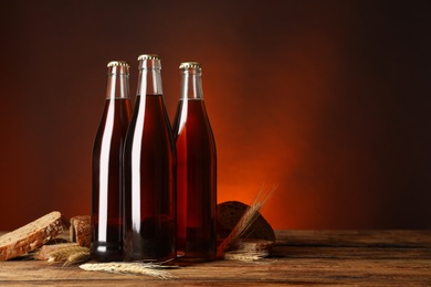 Photo of Bottles of delicious fresh kvass, spikelets and bread on wooden table. Space for text