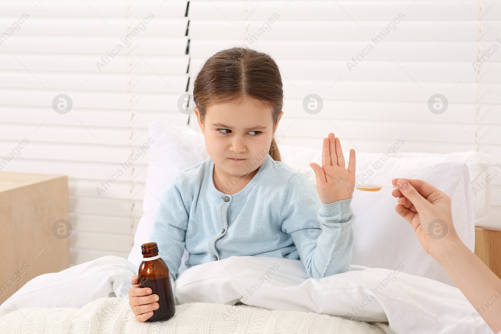 Photo of Daughter refusing to take cough syrup from her mother in bedroom