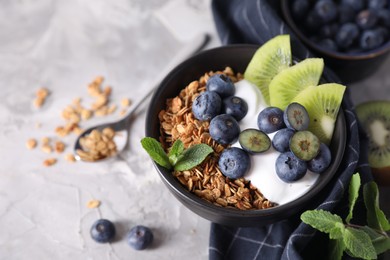 Photo of Tasty granola with yogurt, blueberries and kiwi in bowl on gray table, closeup