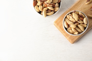 Bowls with tasty Brazil nuts and space for text on white wooden table, top view