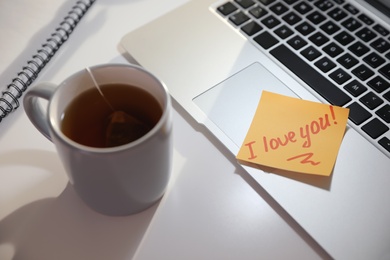 Photo of Sticky note with handwritten text I Love You attached to laptop at workplace. Romantic message