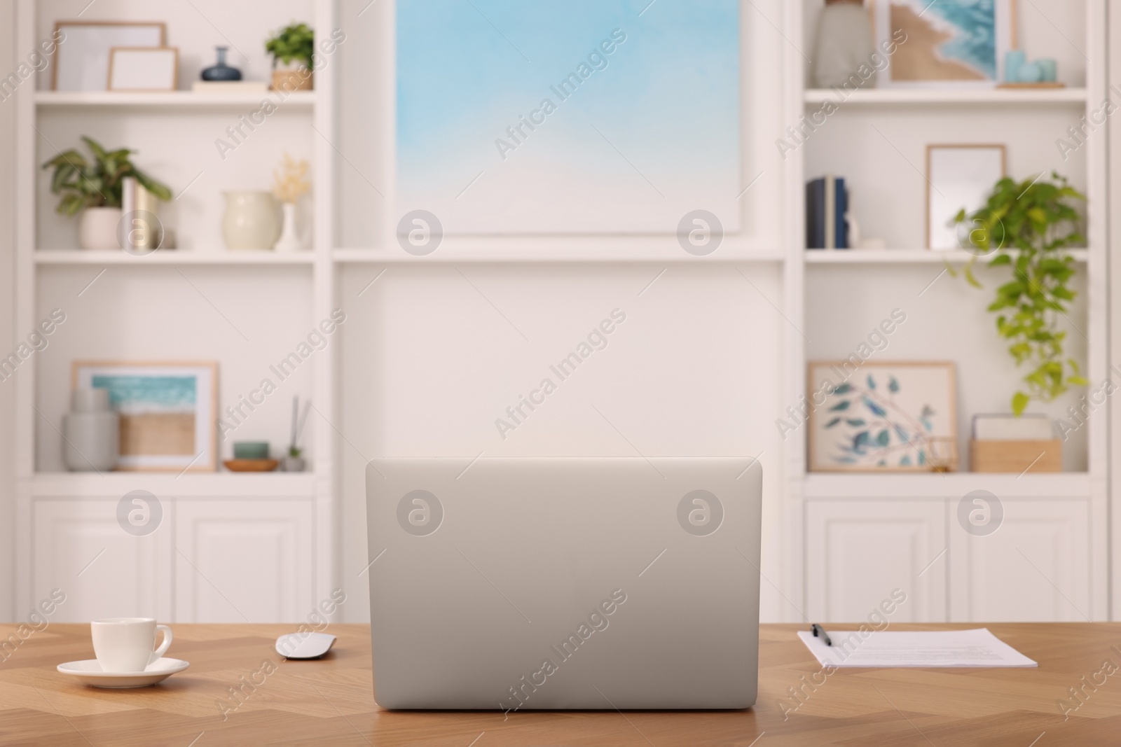 Photo of Interior design. Cosy workplace with laptop on wooden table near abstract picture between shelves