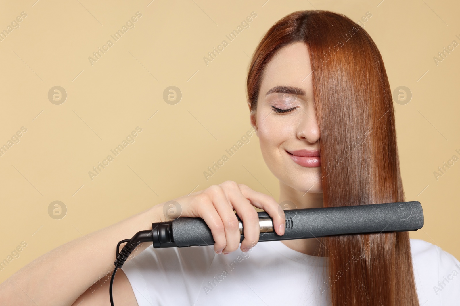 Photo of Beautiful woman using hair iron on beige background, space for text