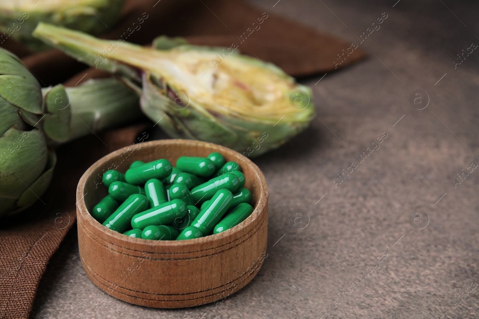 Photo of Bowl with pills and fresh artichokes on brown table, closeup. Space for text