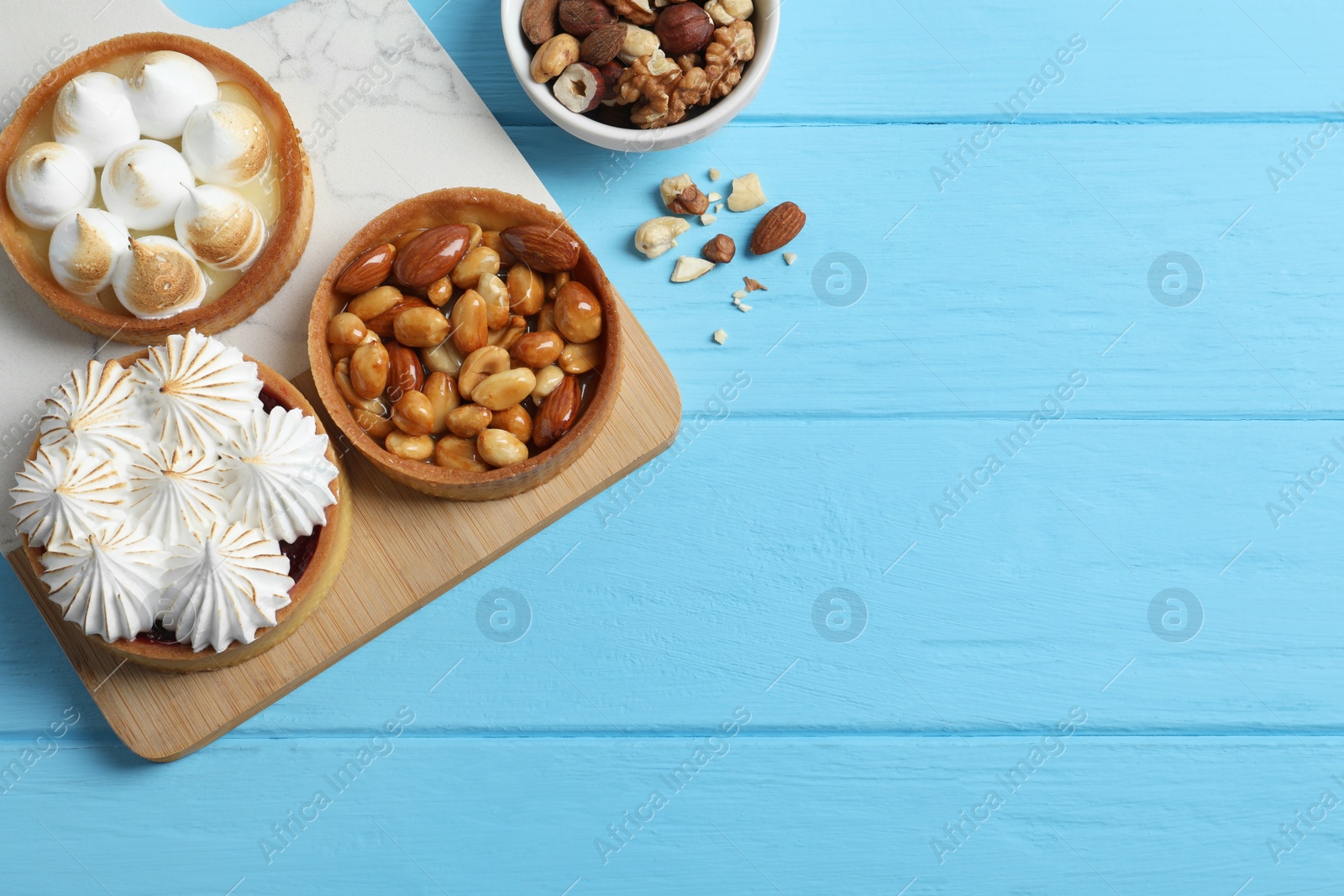 Photo of Different tartlets on light blue wooden table, flat lay with space for text. Delicious dessert