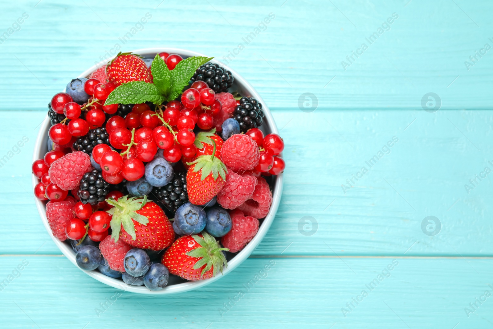 Photo of Mix of different fresh berries and mint in bowl on light blue wooden table, top view. Space for text