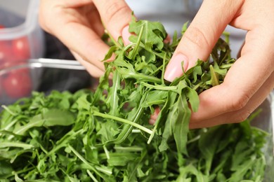 Photo of Woman putting arugula into container, closeup. Food storage
