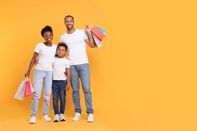 Photo of Family shopping. Happy parents and son with colorful bags on orange background, space for text