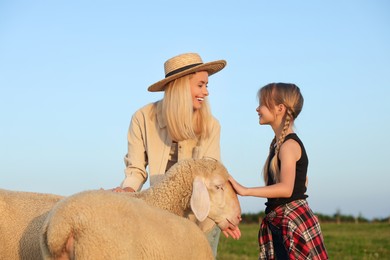 Photo of Mother and daughter feeding sheep on pasture. Farm animals