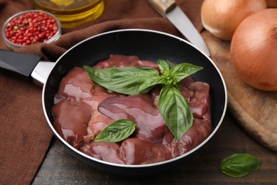 Photo of Raw chicken liver with basil in frying pan on wooden table