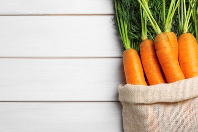 Sack with tasty ripe carrots on white wooden table, top view. Space for text