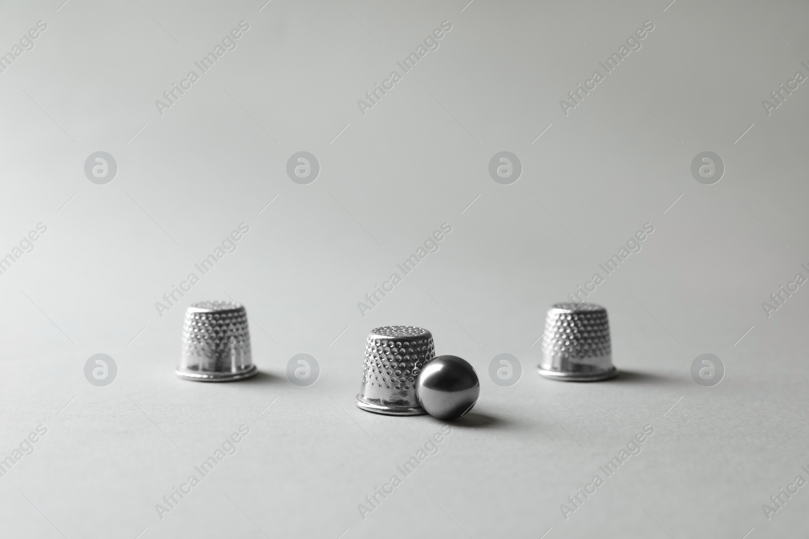 Photo of Metal thimbles and ball on light grey background. Thimblerig game