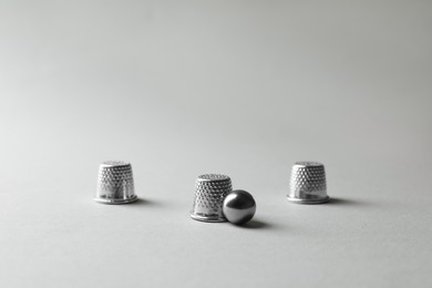 Metal thimbles and ball on light grey background. Thimblerig game