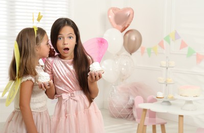 Photo of Cute little girls wearing fairy costumes with delicious cupcakes in decorated room. Space for text