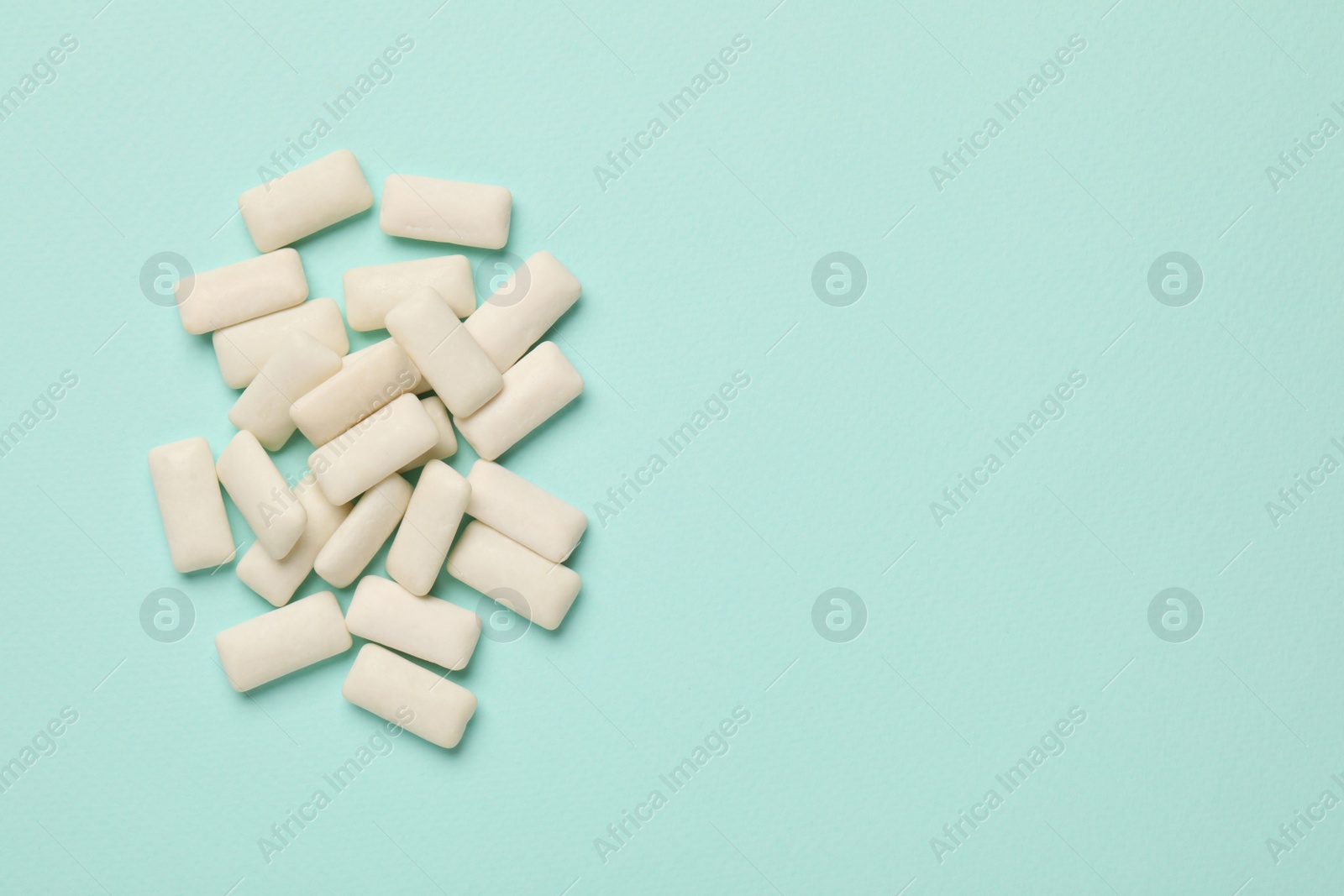Photo of Many chewing gum pieces on turquoise background, flat lay. Space for text