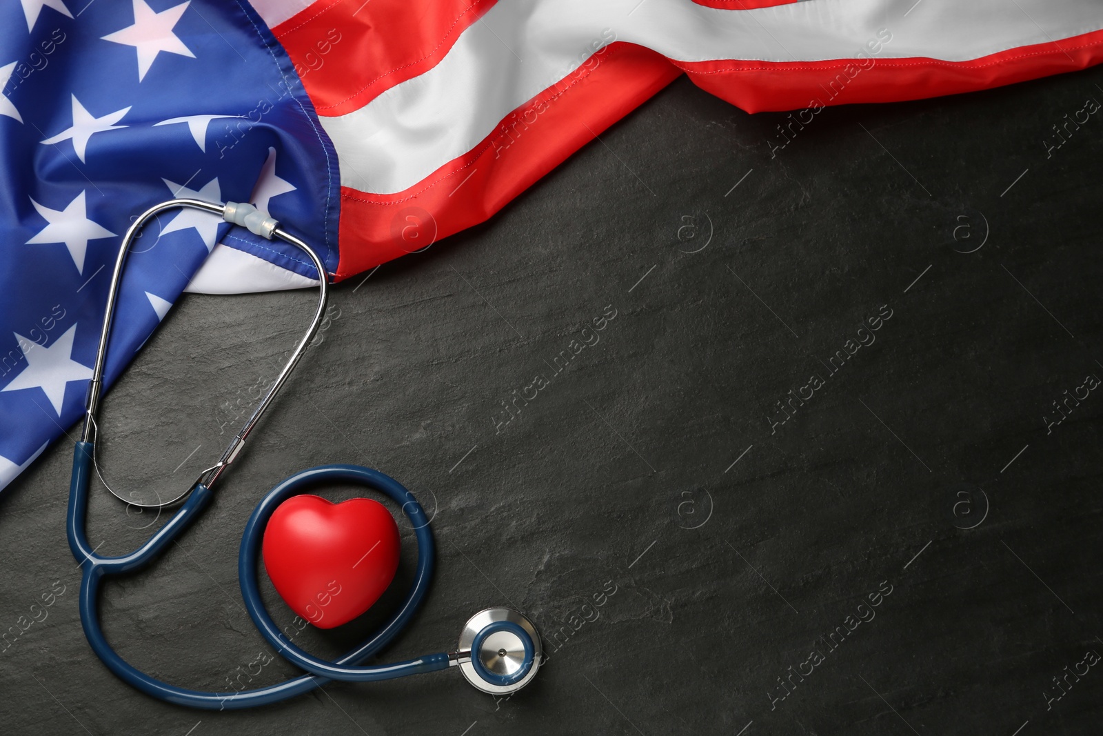 Photo of American flag, heart and stethoscope on black table, flat lay. Space for text