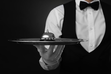 Photo of Butler holding metal tray with service bell on black background, closeup