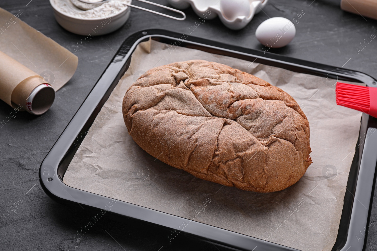 Photo of Baking pan with bread, parchment paper and ingredients on black slate background