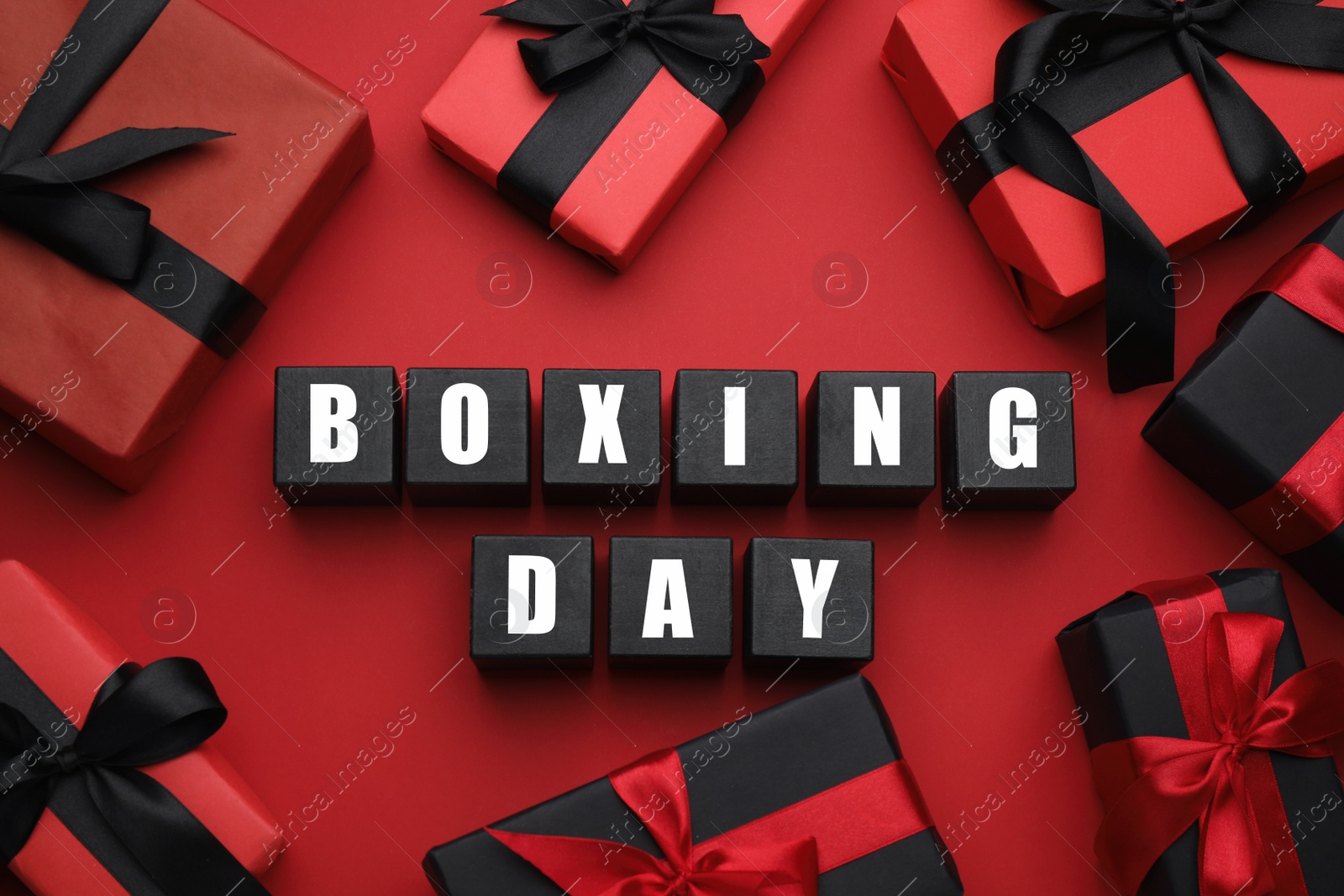 Photo of Black wooden cubes with text Boxing Day and gifts on red background, flat lay. Sale concept