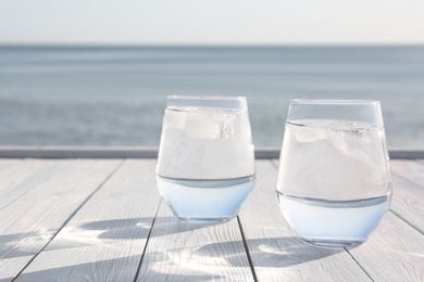 Photo of Wooden table with glasses of refreshing drink on hot summer day outdoors