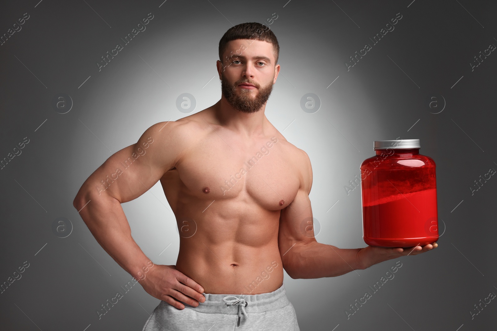 Photo of Young man with muscular body holding jar of protein powder on grey background