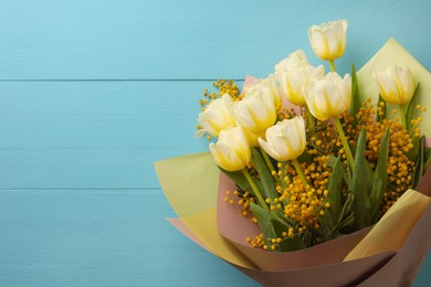 Bouquet with beautiful tulips and mimosa flowers on light blue wooden table, top view. Space for text