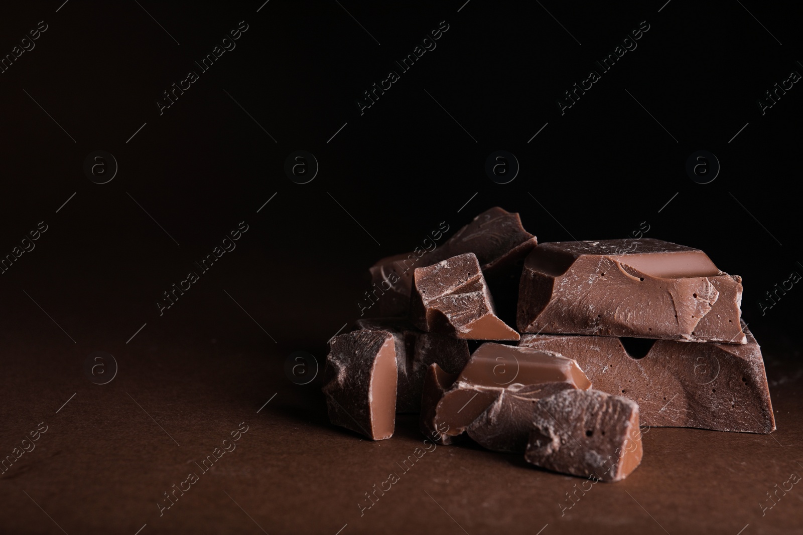 Photo of Pieces of milk chocolate on brown table. Space for text