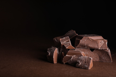 Photo of Pieces of milk chocolate on brown table. Space for text