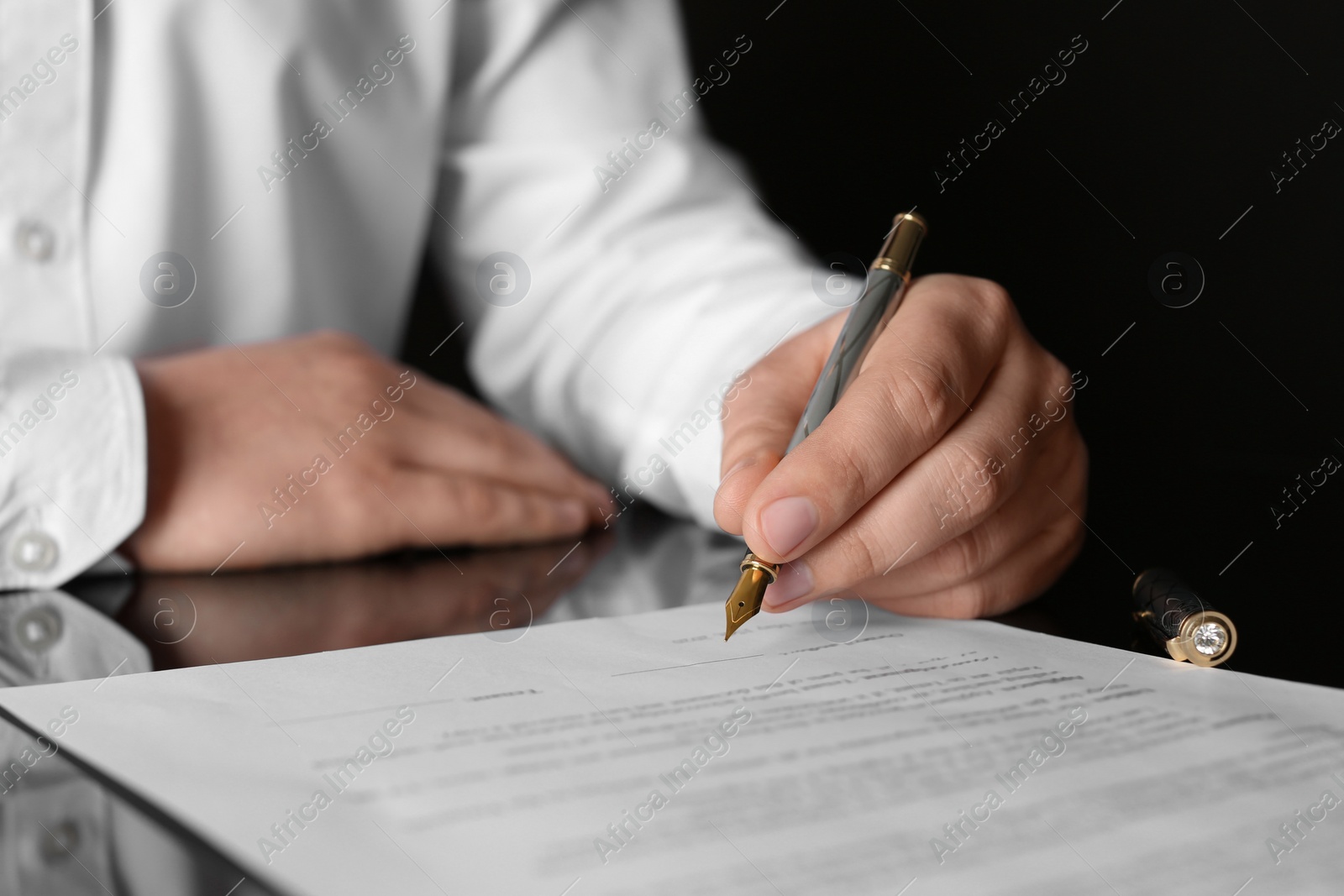 Photo of Notary signing document at black table, closeup