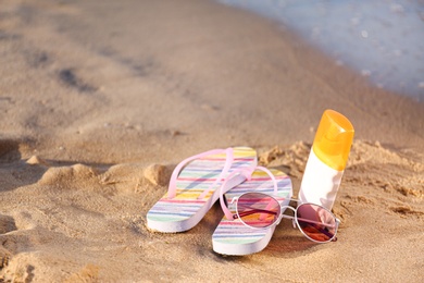 Photo of Flip flops and beach accessories on sand near sea. Space for text