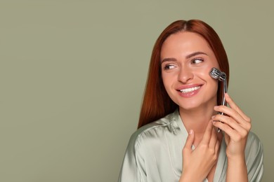 Photo of Young woman massaging her face with metal roller on green background, space for text