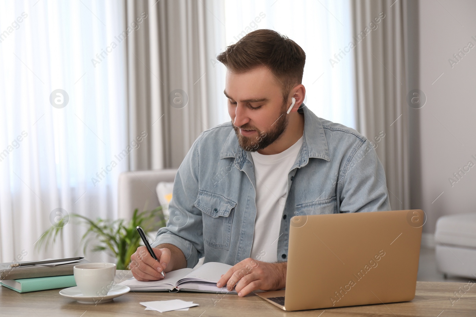 Photo of Young man taking notes during online webinar at table indoors