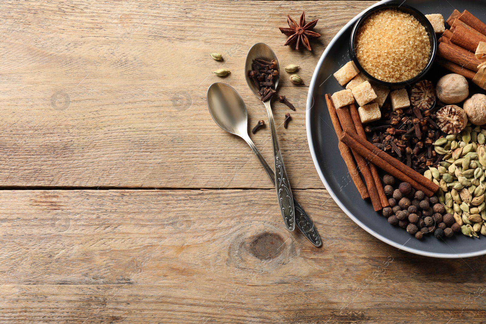 Photo of Plate with different aromatic spices and spoons on wooden table, flat lay. Space for text