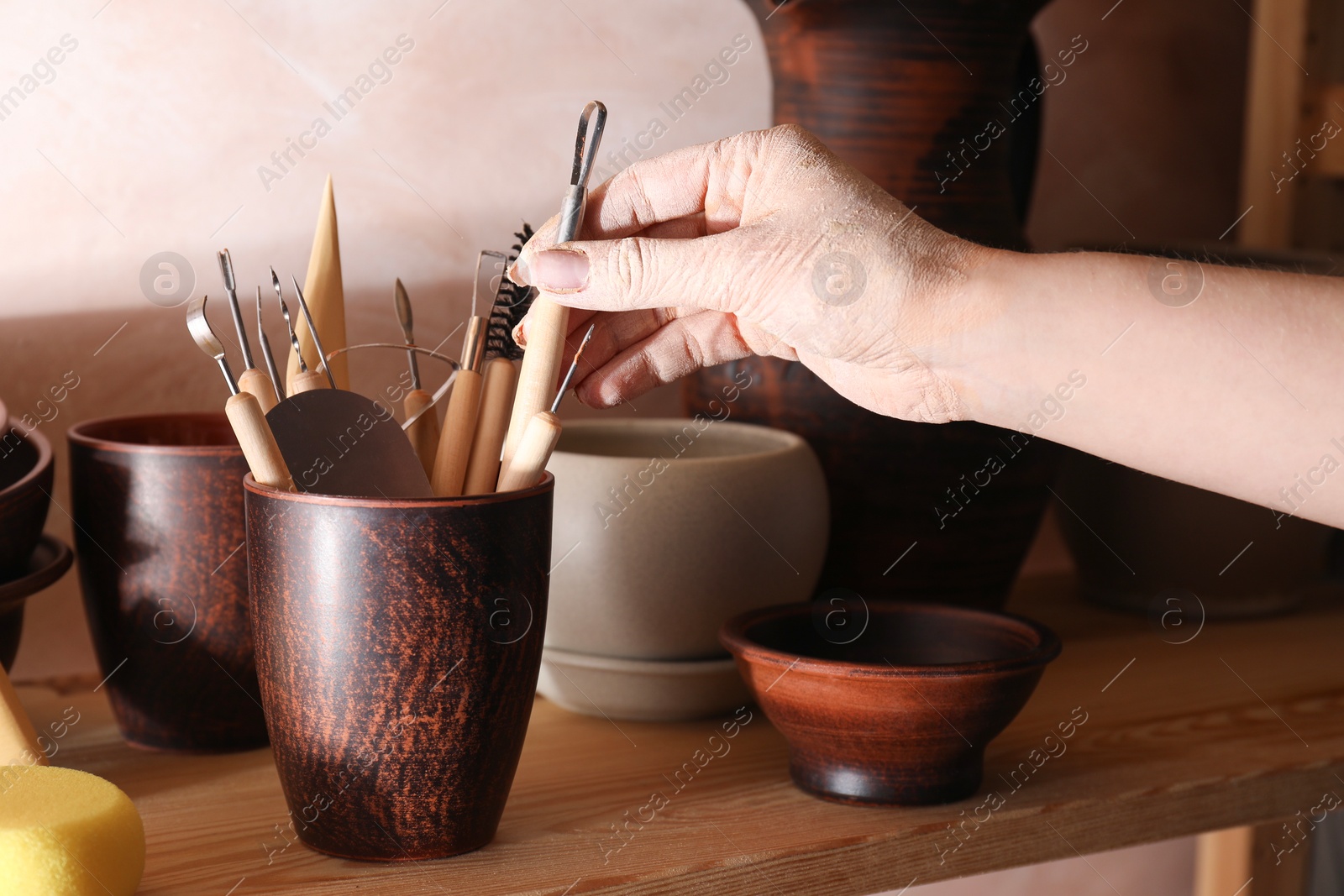 Photo of Woman taking clay crafting tool from cup in workshop, closeup