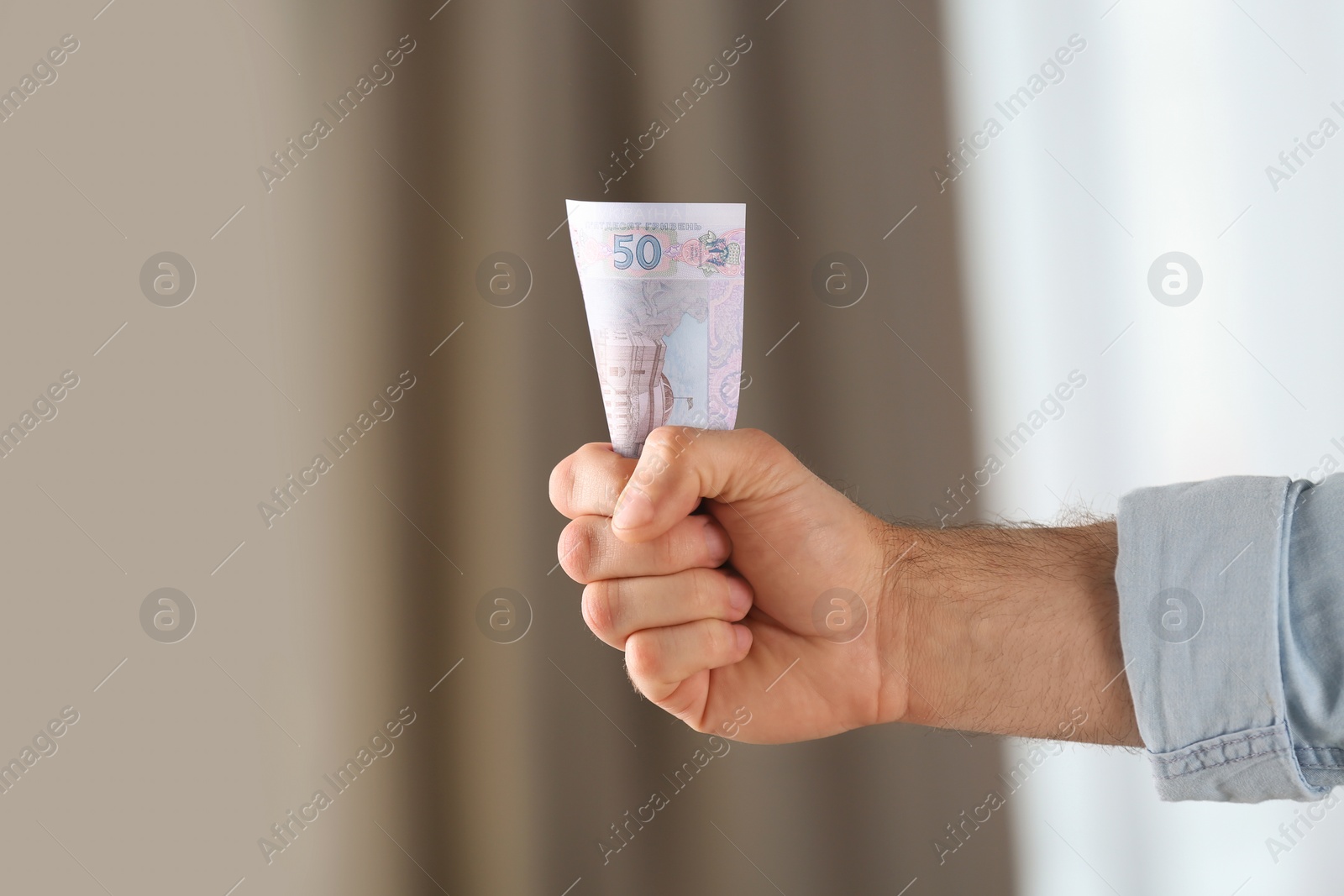 Photo of Man holding 50 Ukrainian Hryvnias banknote against blurred background, closeup with space for text. International relationships