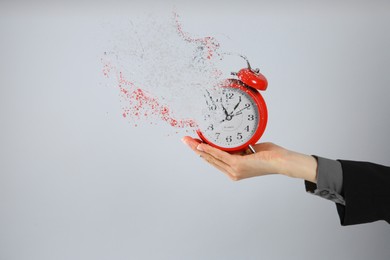 Image of Time is running out. Woman holding vanishing red alarm clock against light grey background, closeup
