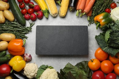 Fresh ripe vegetables and blank slate board on grey table, flat lay. Space for text