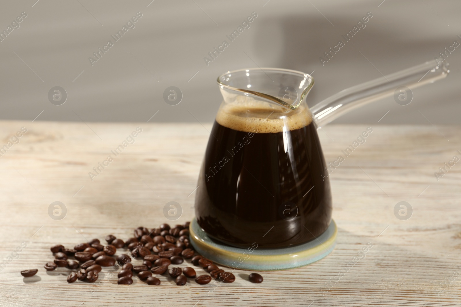 Photo of Glass turkish coffee pot with hot drink and beans on wooden table