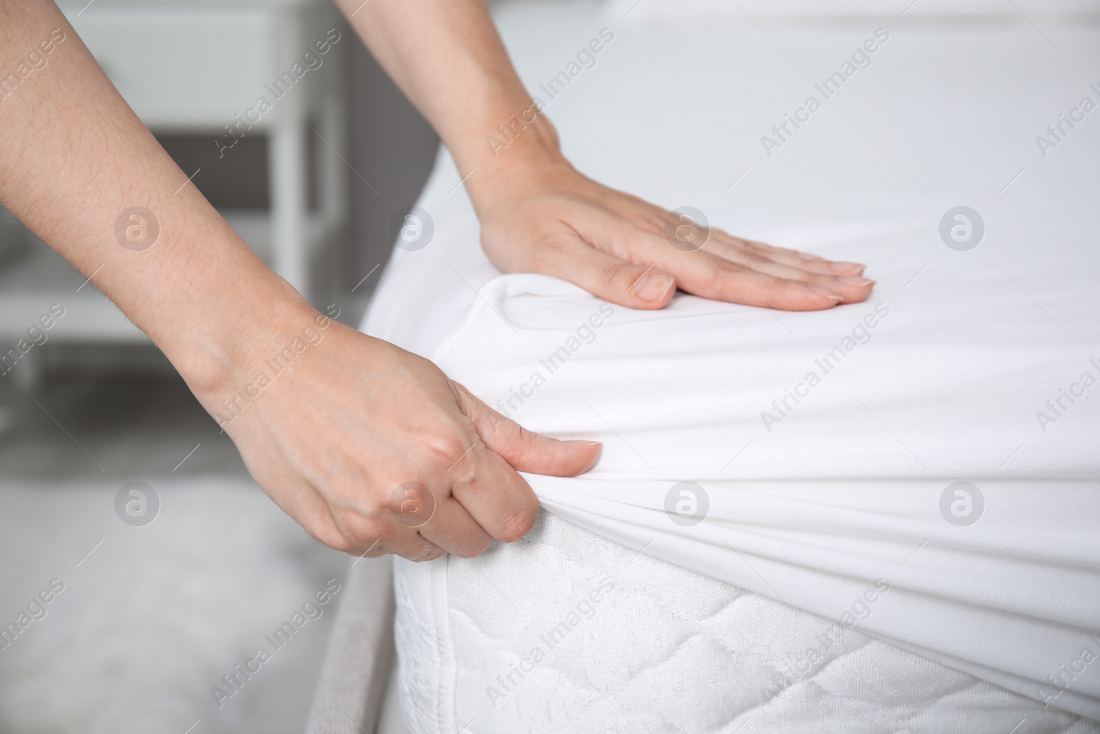 Photo of Woman putting white fitted sheet over mattress on bed indoors, closeup