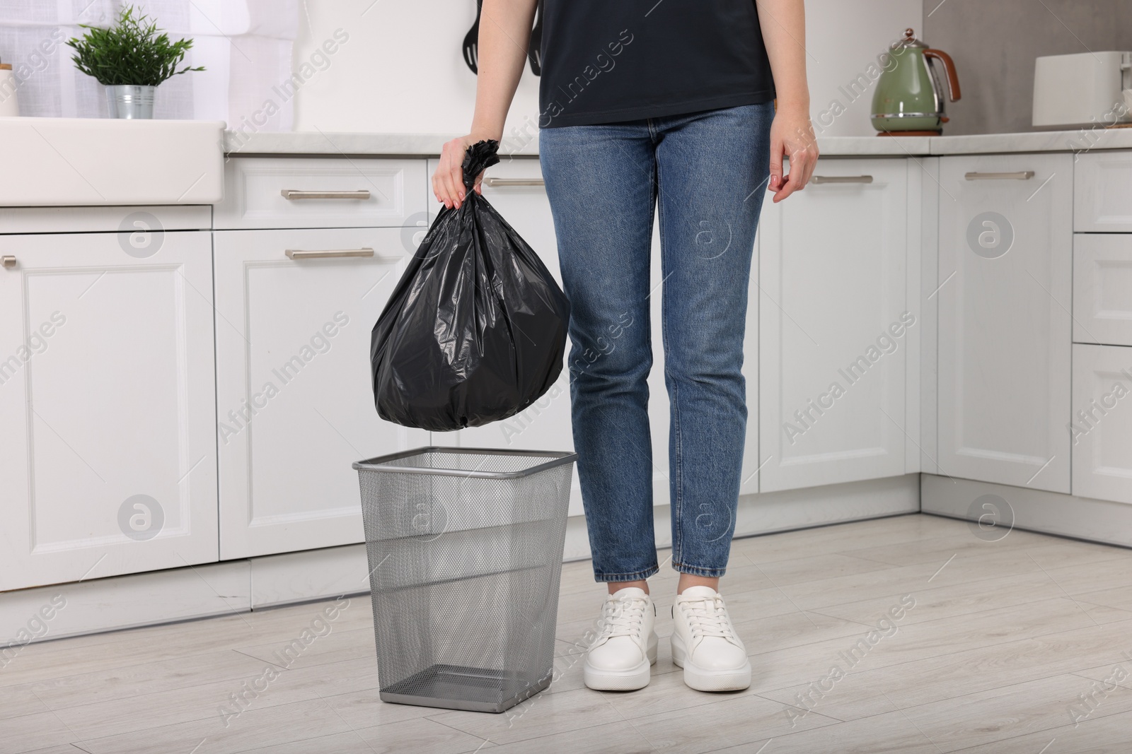 Photo of Woman taking garbage bag out of trash bin in kitchen, closeup