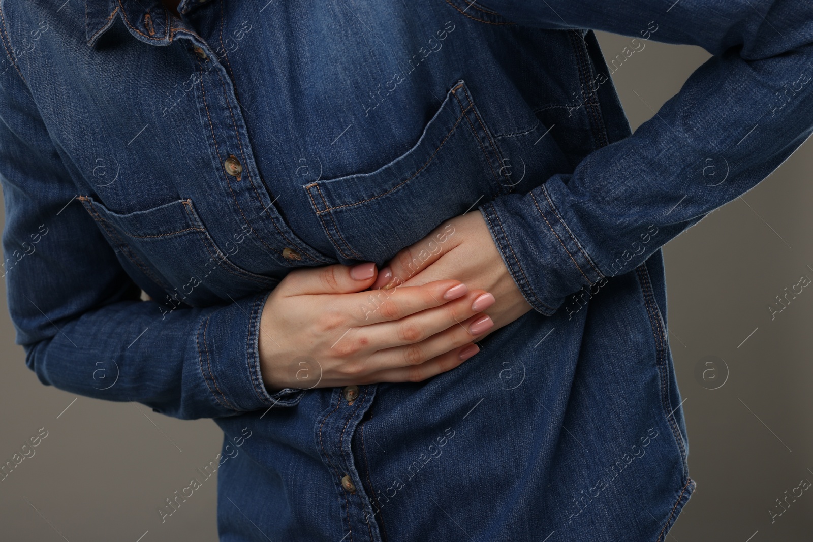 Photo of Woman suffering from stomach pain on grey background, closeup