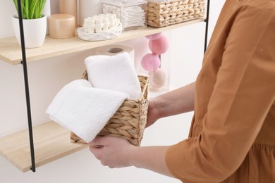 Bath accessories. Woman with basket of clean towels indoors, closeup