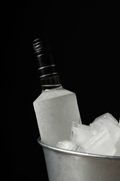 Photo of Bottle of vodka in metal bucket with ice on black background